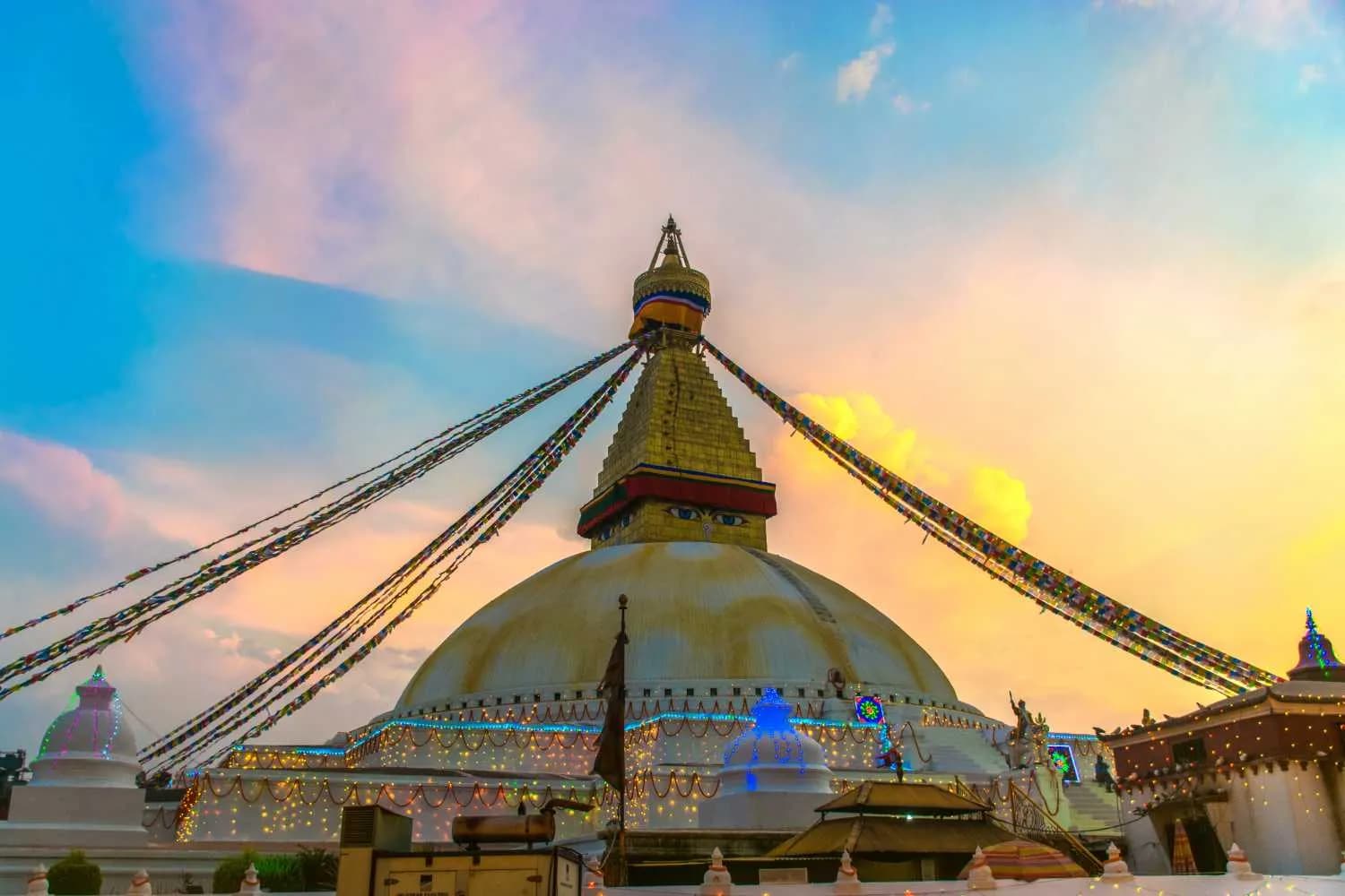 Sunset view of the Boudhanath Stupa in Kathmandu Nepal featuring the iconic Buddha eyes colorful prayer flag and decorative evening lights against a pastel sky
