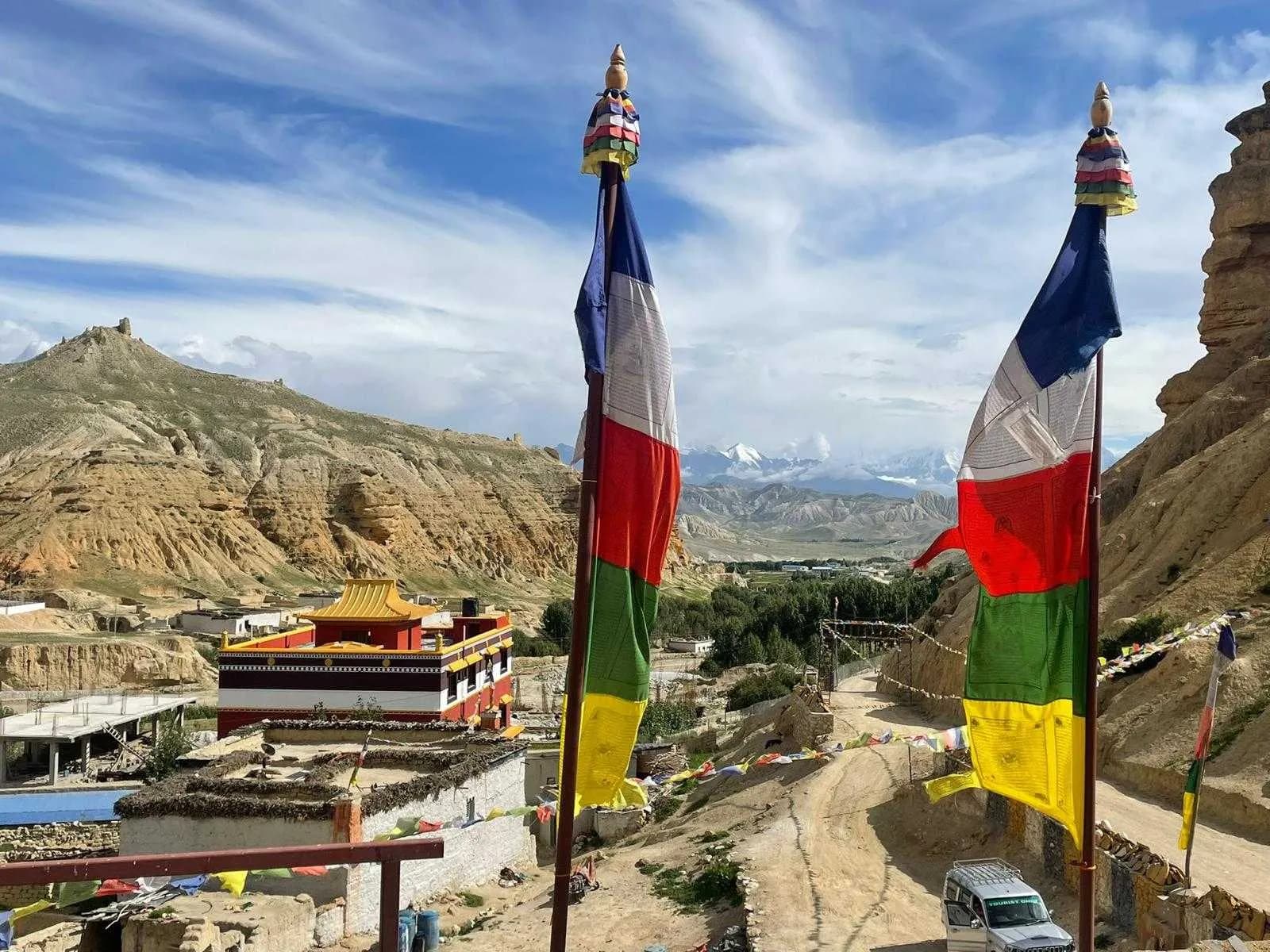 Tall vertical prayer flags overlooking a dusty road and a traditional village nestled in the valley Tall vertical prayer flags overlooking a dusty road and a traditional village nestled in the valley