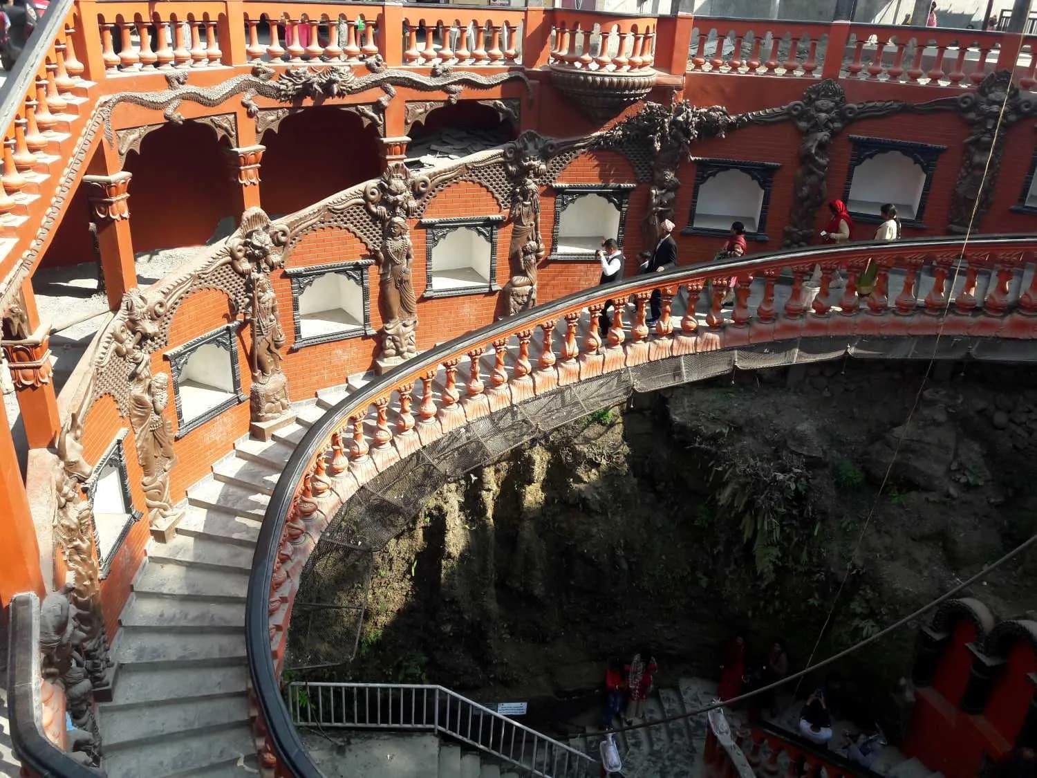 Ornate spiral staircase entrance to Gupteshwor Mahadev Cave featuring intricate carvings and red brick walls Ornate spiral staircase entrance to Gupteshwor Mahadev Cave featuring intricate carvings and red brick walls